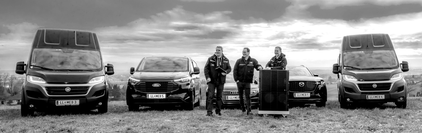 Teamfoto von MEB Veranstaltungstechnik mit Fahrzeugflotte und Eventtechnik-Equipment – Einsatzbereit für Veranstaltungen in ganz Österreich